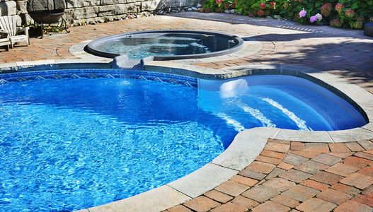 A large swimming pool with stairs and a hot tub in the backyard.