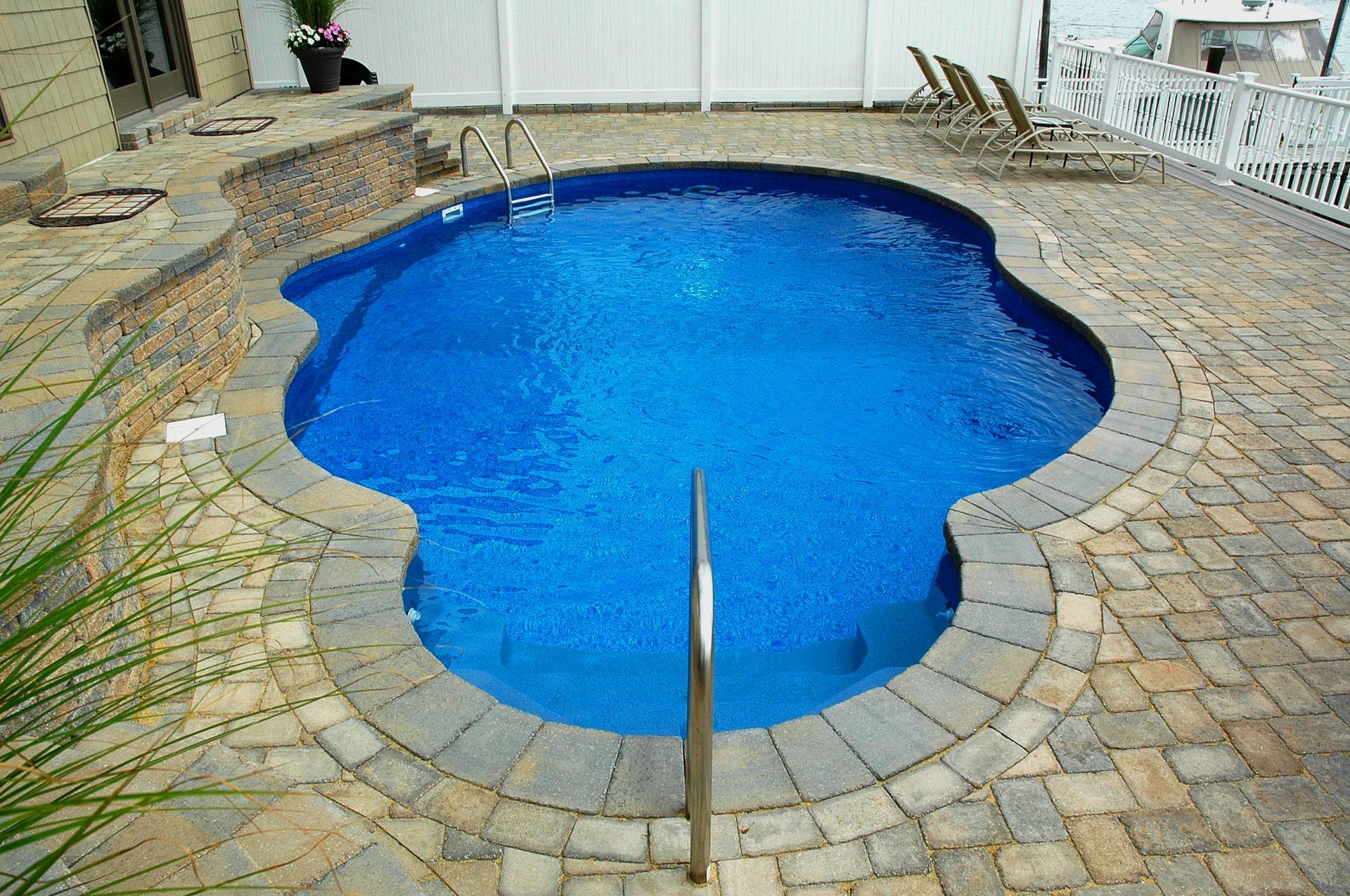 A large blue swimming pool is surrounded by bricks and chairs.