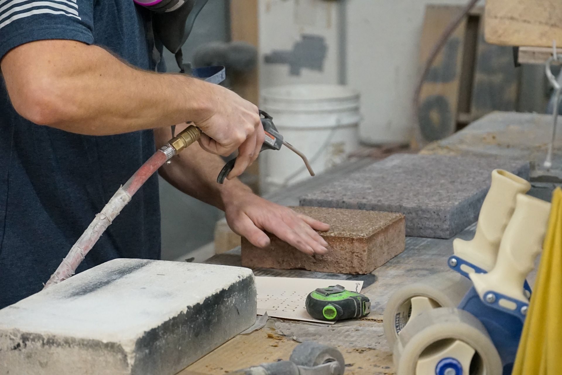 A person using an air gun to clean a block on a workbench in a workshop.