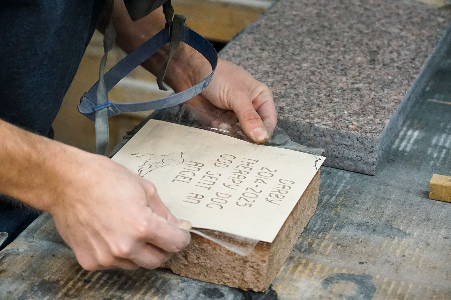 Person places stencil on stone block, preparing for engraving. Another stone is nearby.