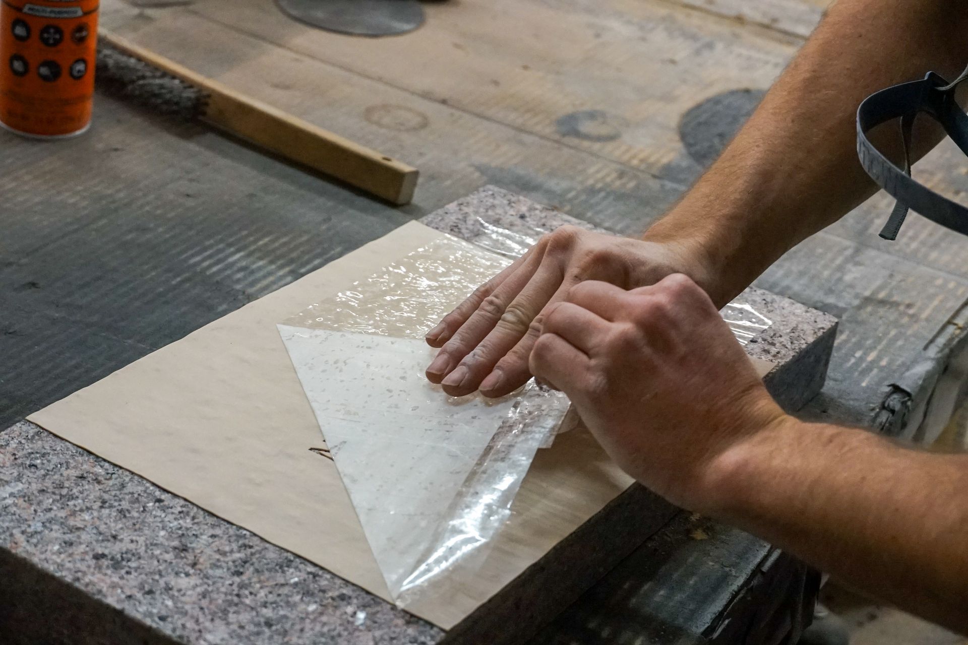 Hands applying a transparent adhesive sheet to a triangular paper pattern on a granite surface.