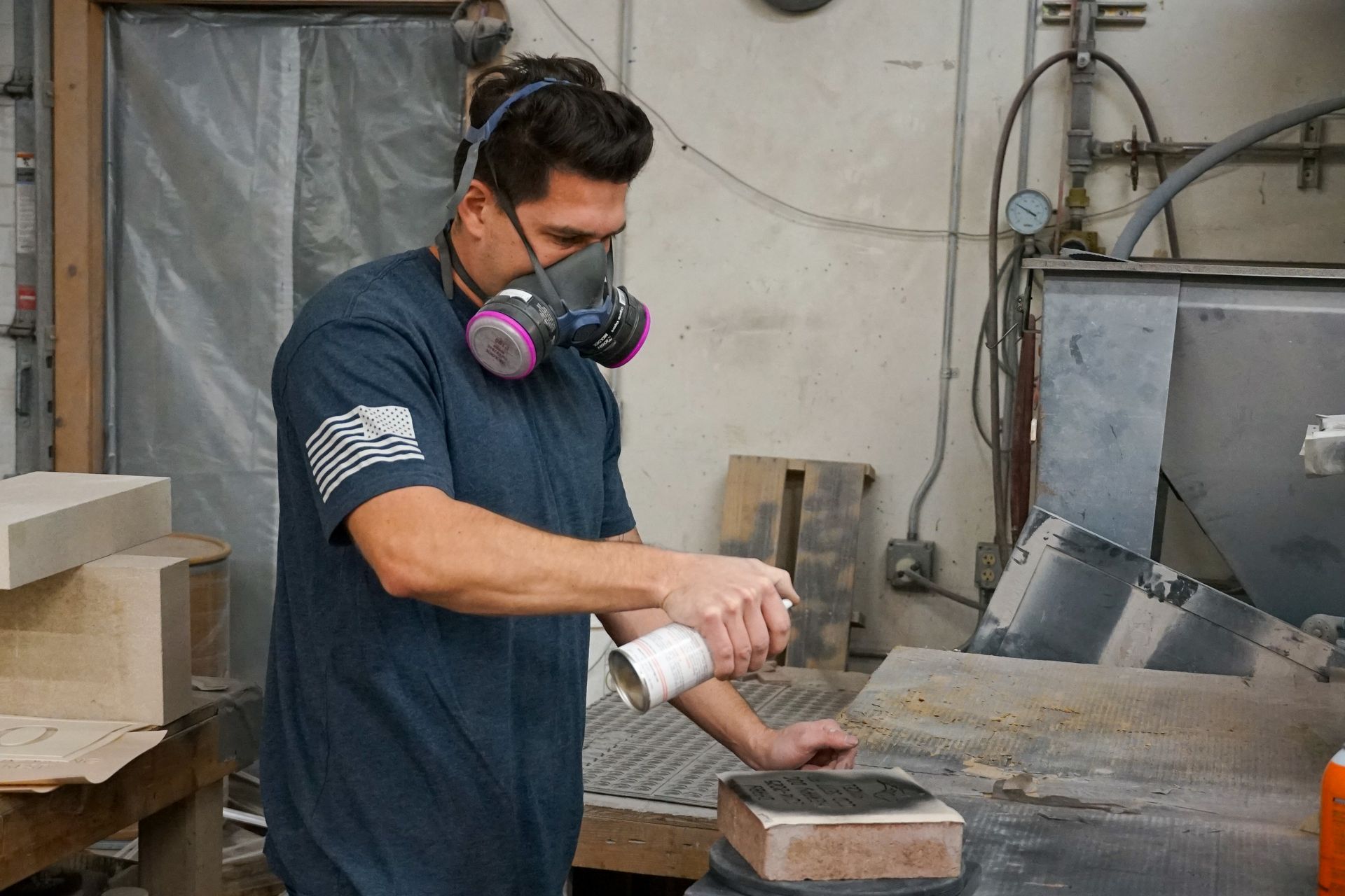 Man spraying something while wearing a respirator in a workshop.
