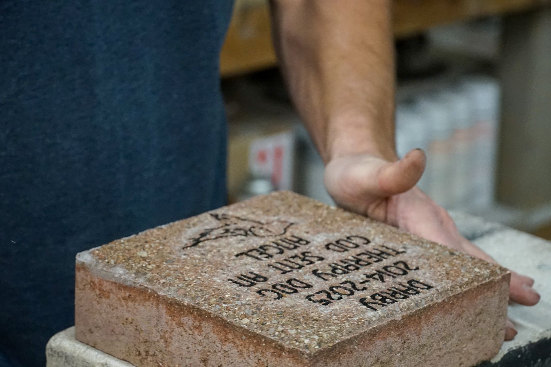 Person holding a brick engraved with text, likely for a memorial.