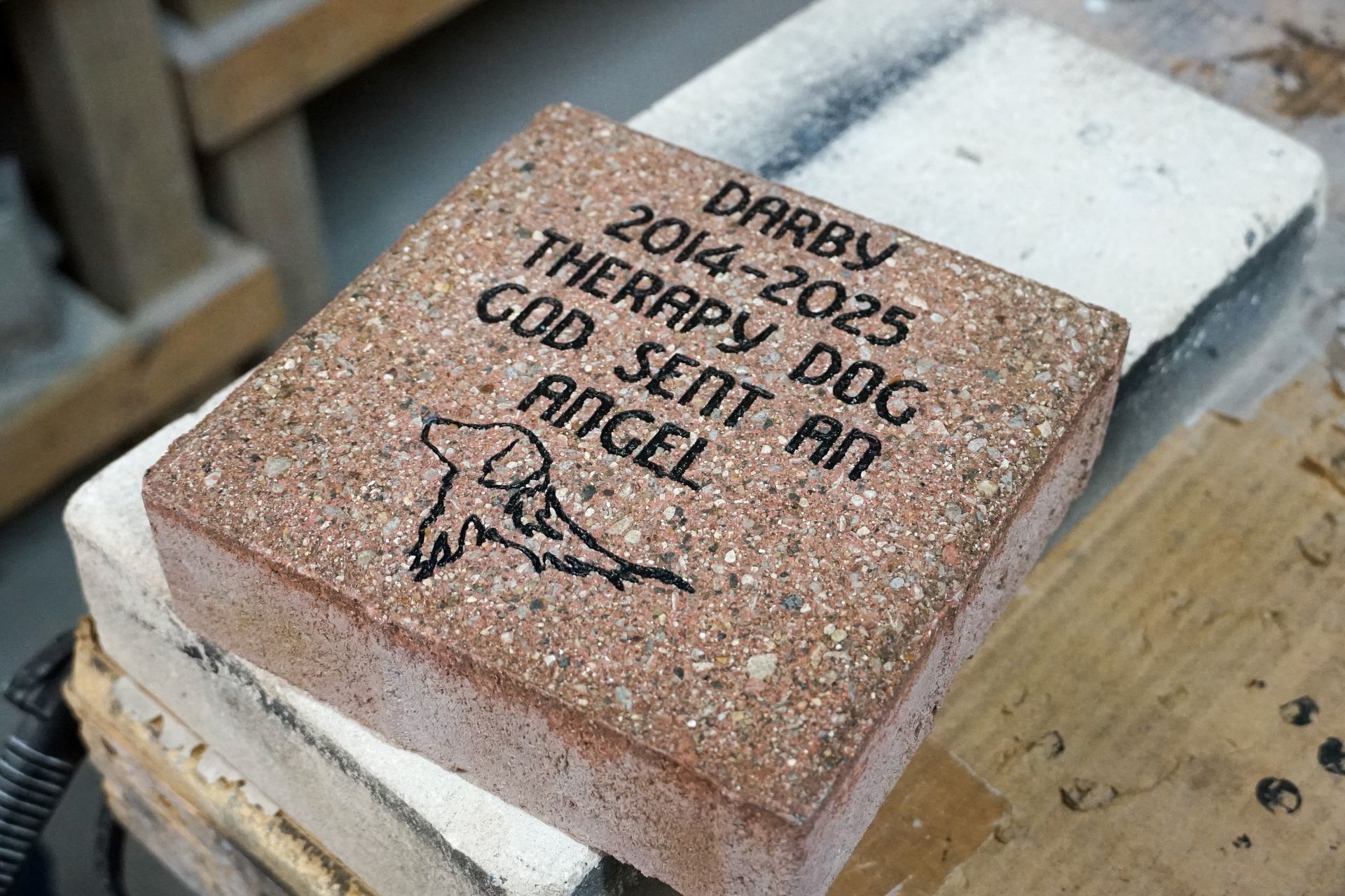 Gravestone brick with engraved name, dates, and dog drawing.