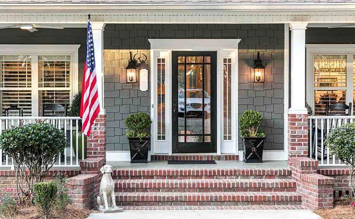 Front porch of a house with brick steps, a black door, and potted plants. American flag on the left.