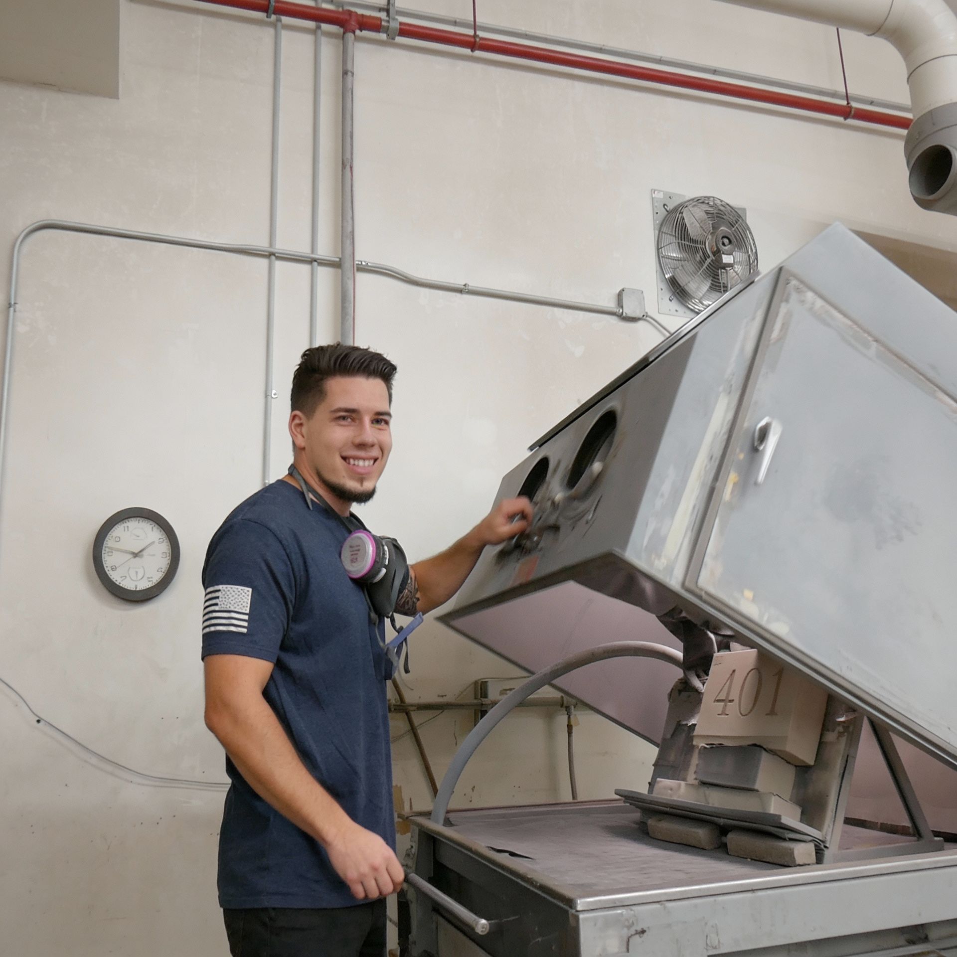 Man in workshop with mask smiles, operating sandblasting equipment.