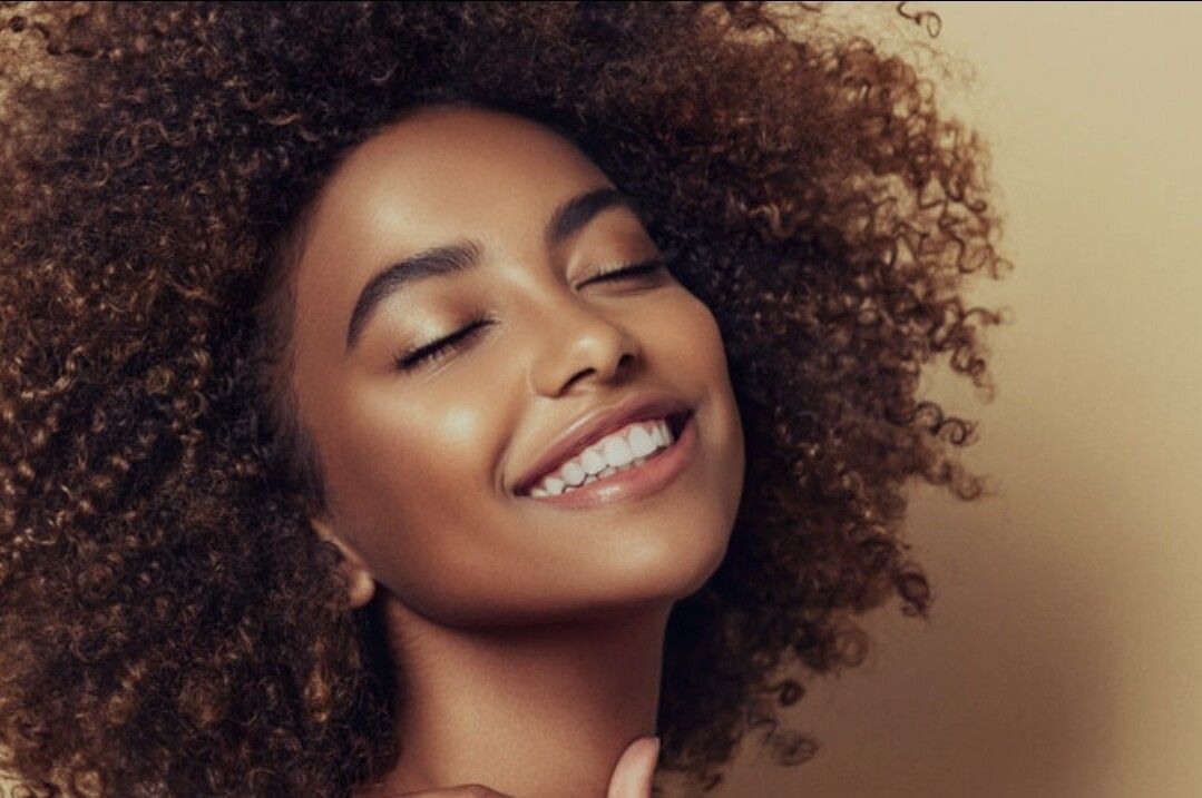 A woman is smiling while holding a tooth color chart in front of her teeth.