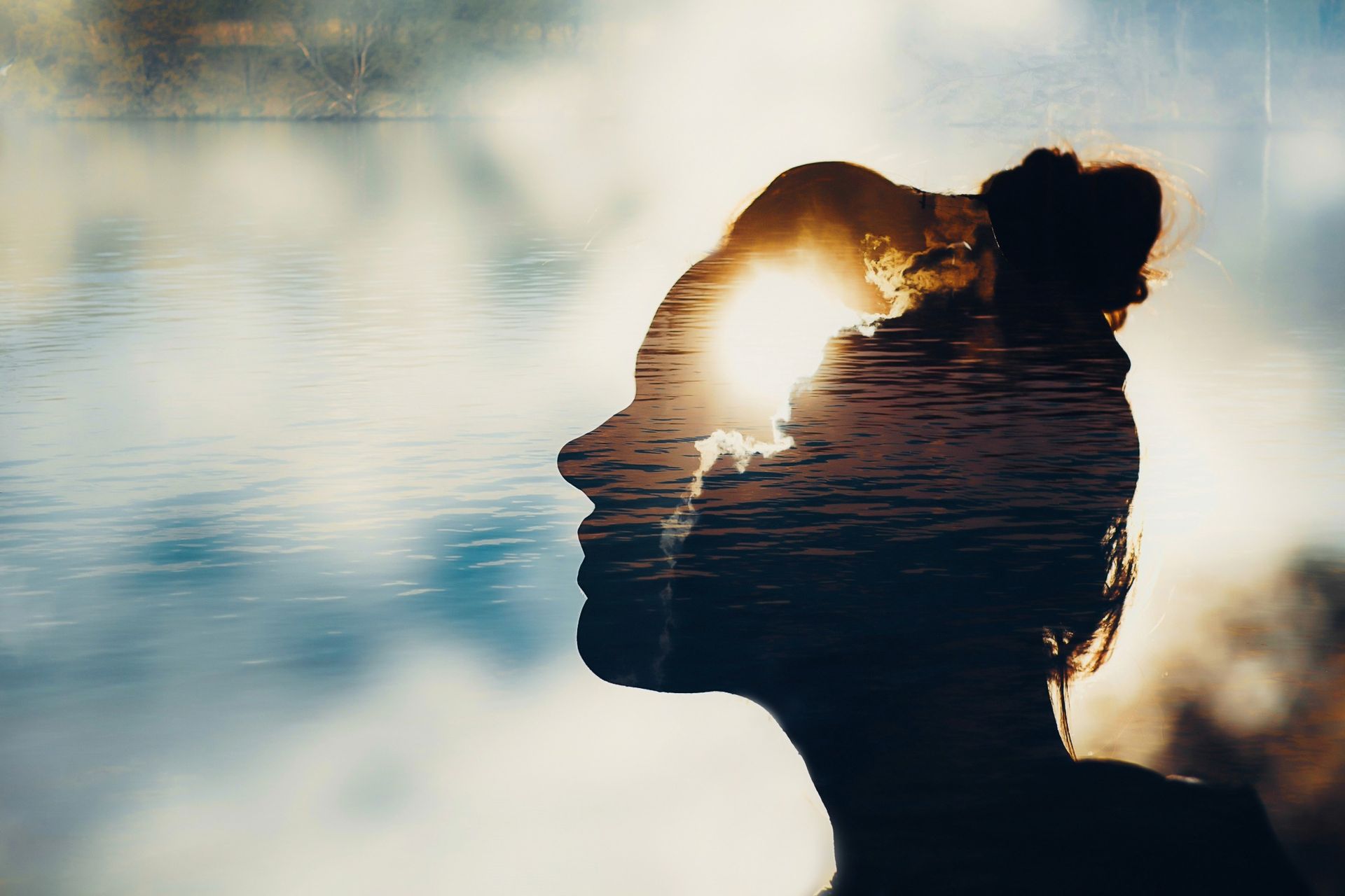 Silhouette of person with a lake scene layered within the head, sun shining through.