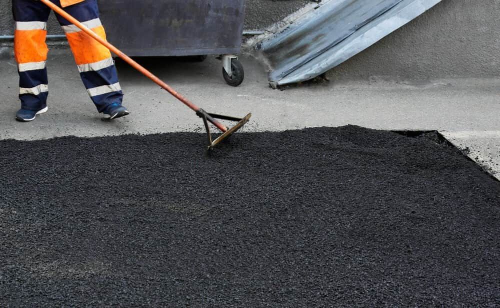 A Man Is Raking Asphalt On The Ground With A Rake — Territory Bitumen Services In Tivendale, NT