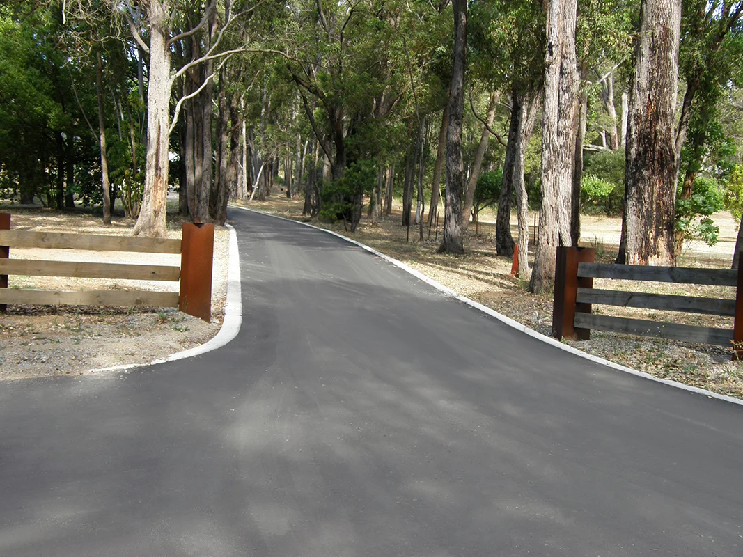 A Road Leads Down A Driveway With A Brown Fence — Territory Bitumen Services In Tivendale, NT