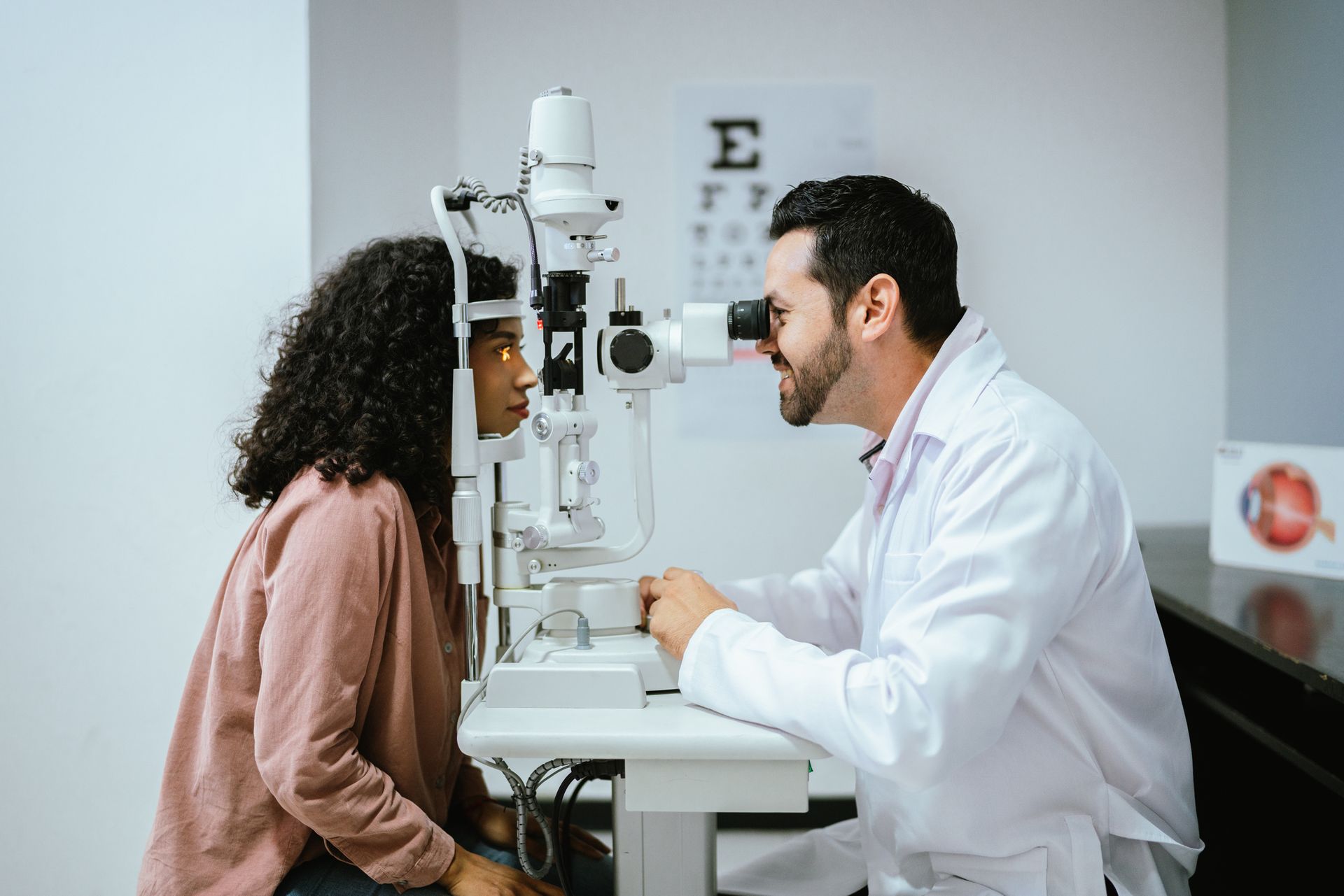 Male eye doctor conducting detailed eye checkup using slit lamp on young woman at clinic.