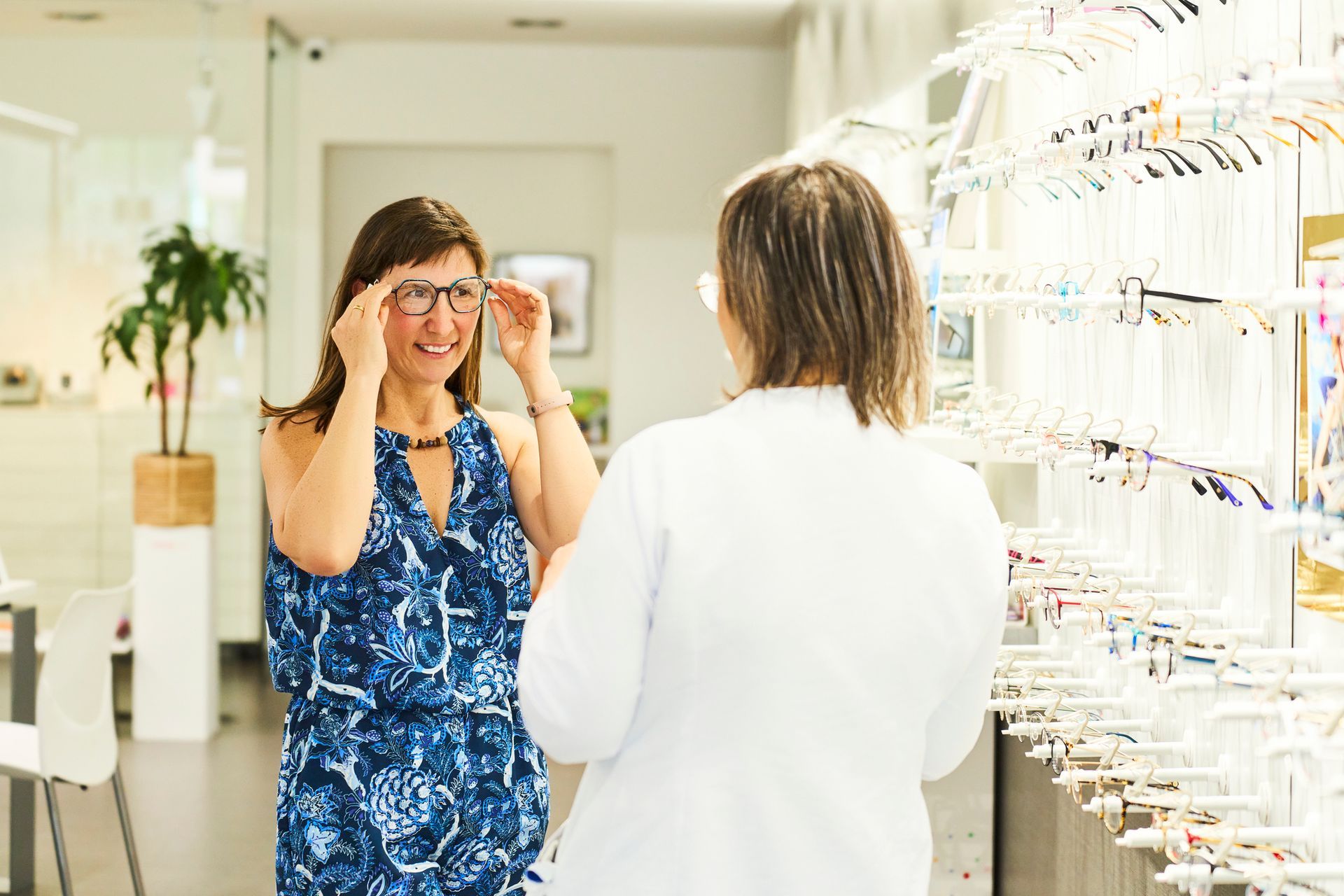 Rear view of a doctor of optometry in a lab coat, standing and talking to her smiling client.