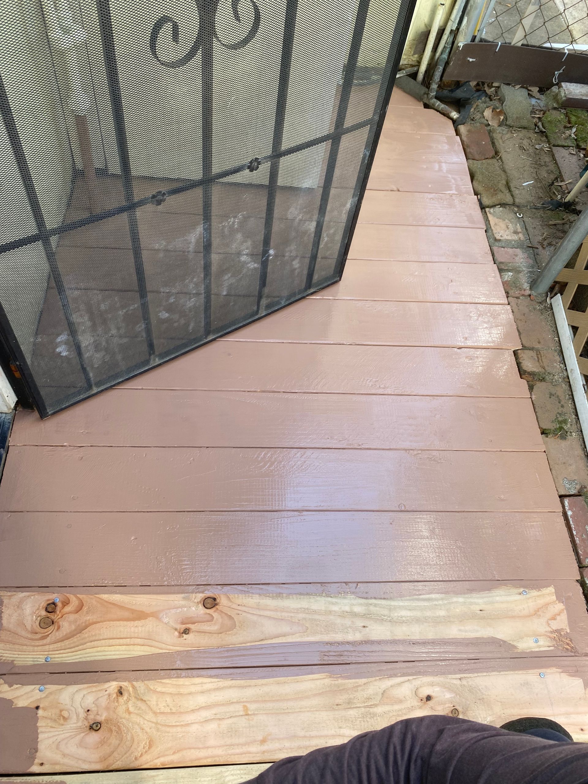 A person is standing on a wooden deck next to a screen door.