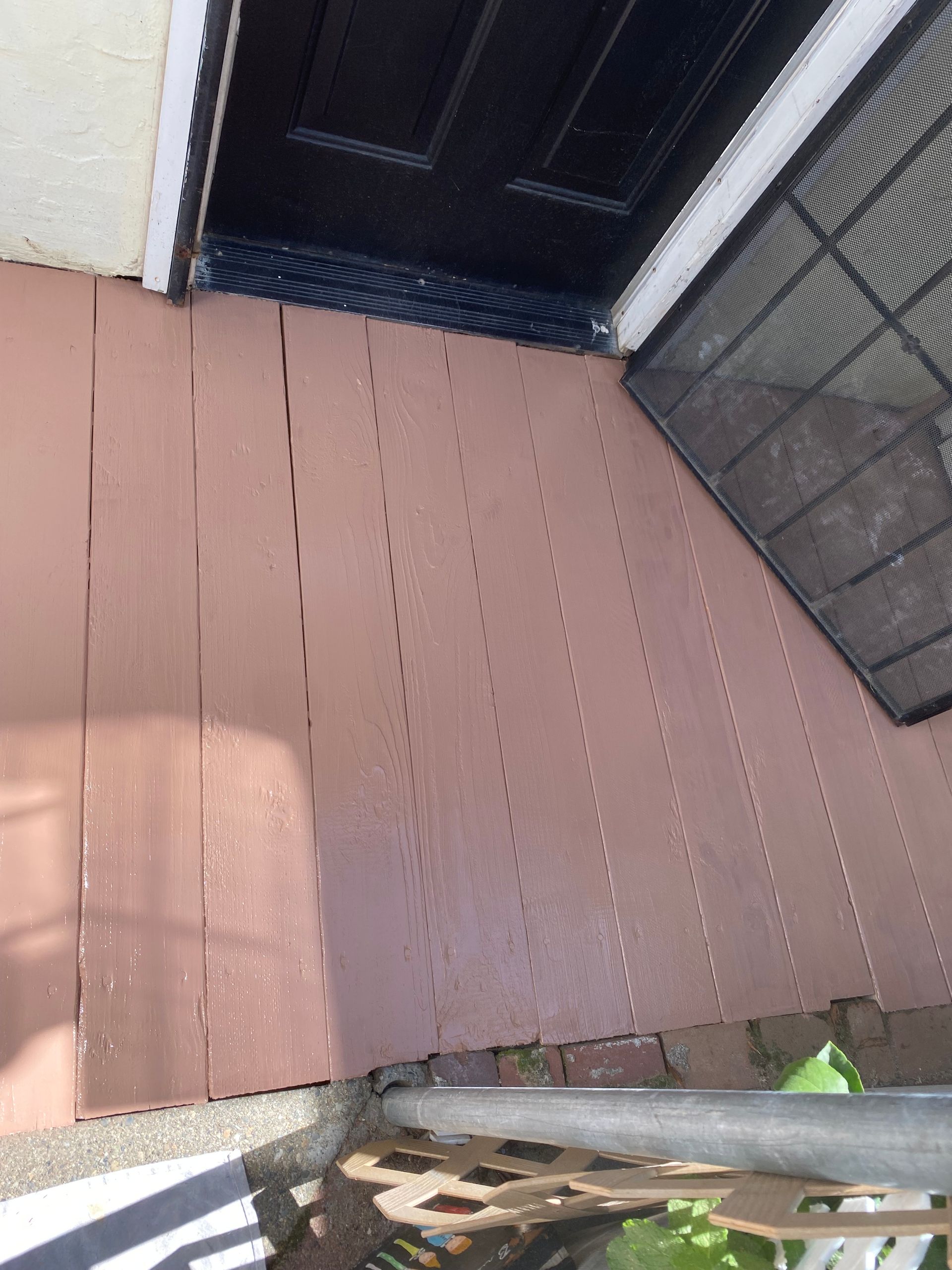 A wooden porch with a black door and a screen door