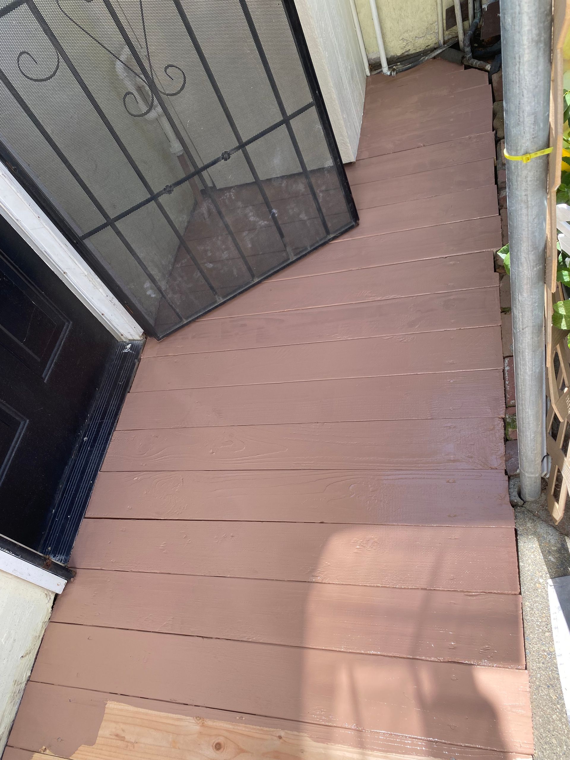 A wooden walkway leading to a house with a screen door.