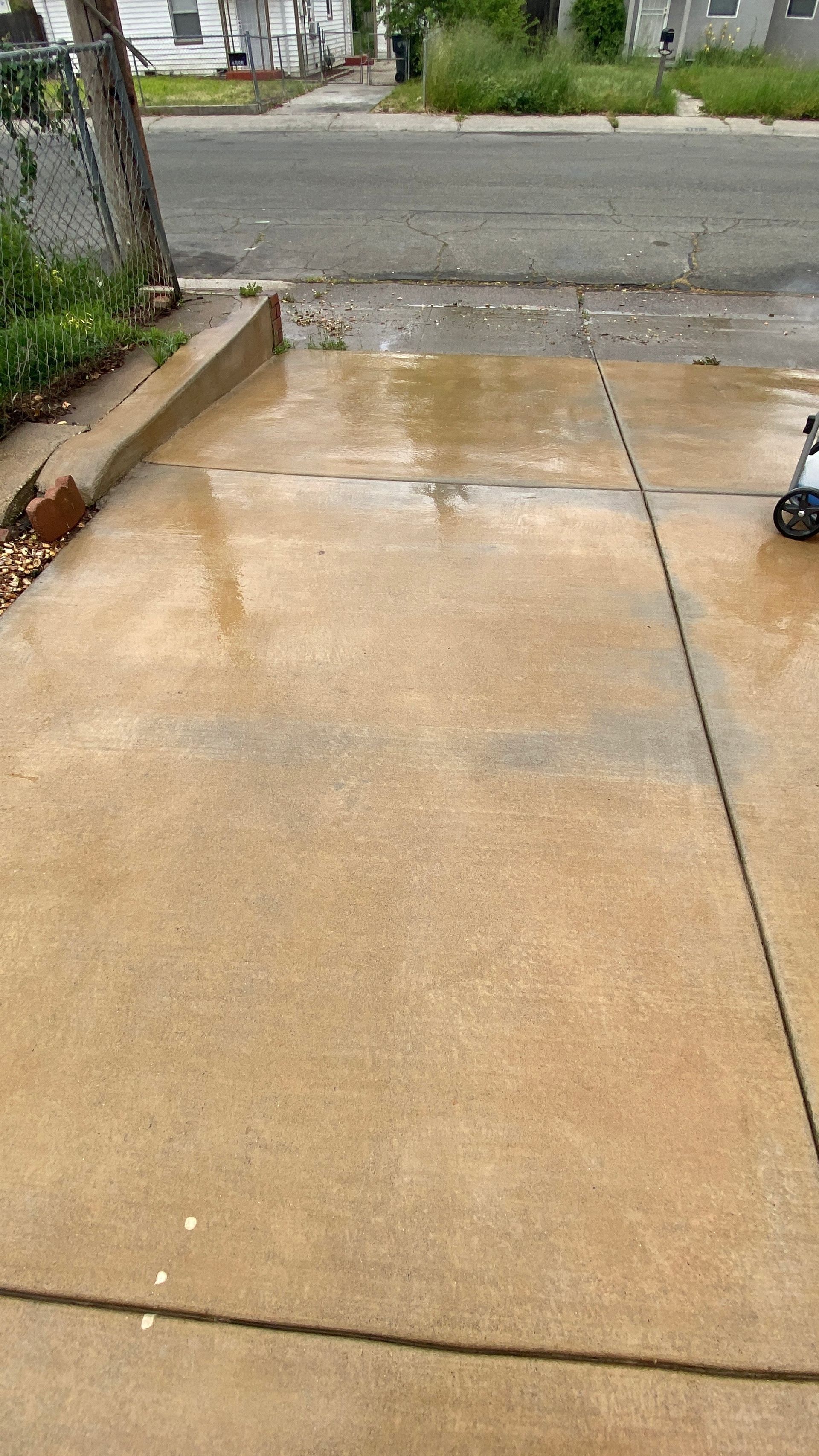 A person is cleaning a concrete driveway with a pressure washer.