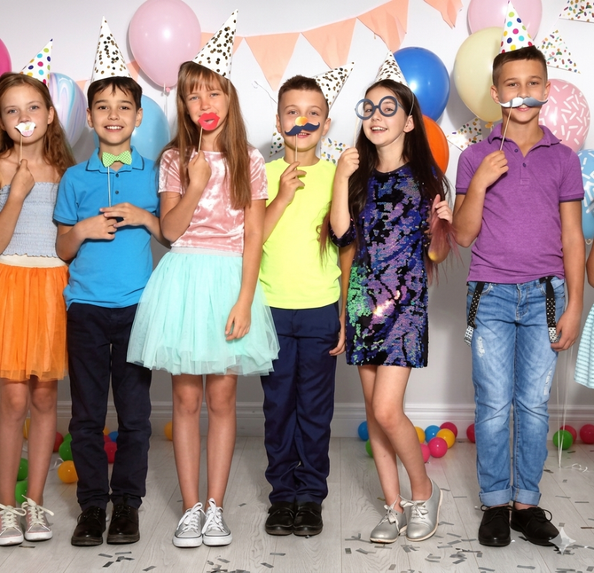 Children in party hats posing in front of balloons at a birthday celebration