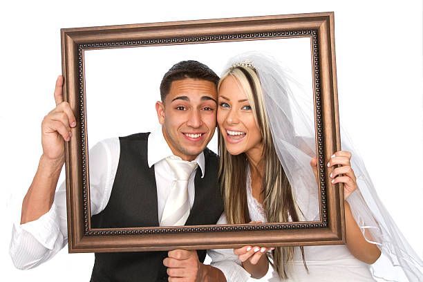 Smiling couple posing inside a large wooden picture frame on a white background