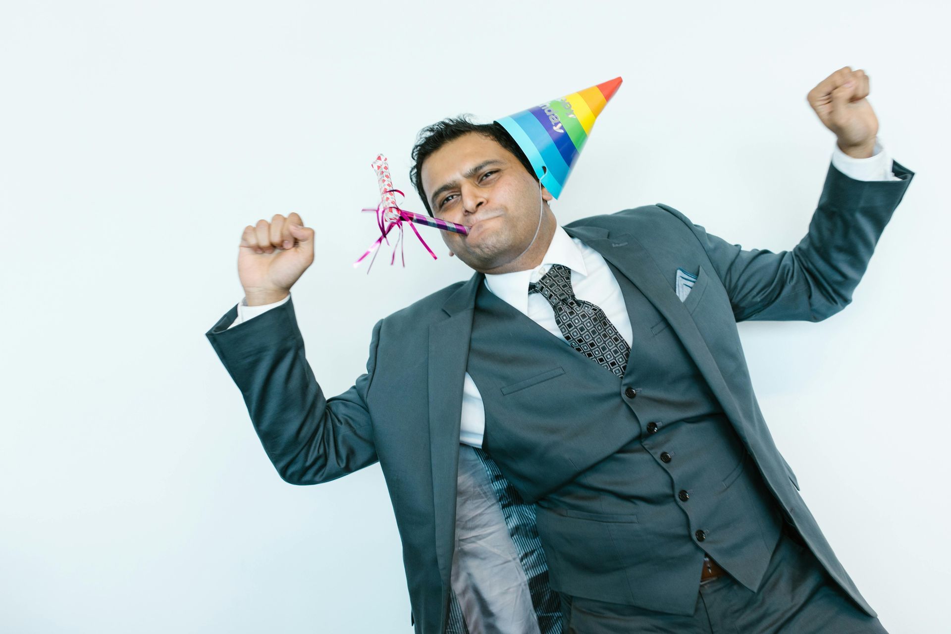 Man in a suit wearing a colorful party hat, raising both fists in celebration, with confetti on a white background