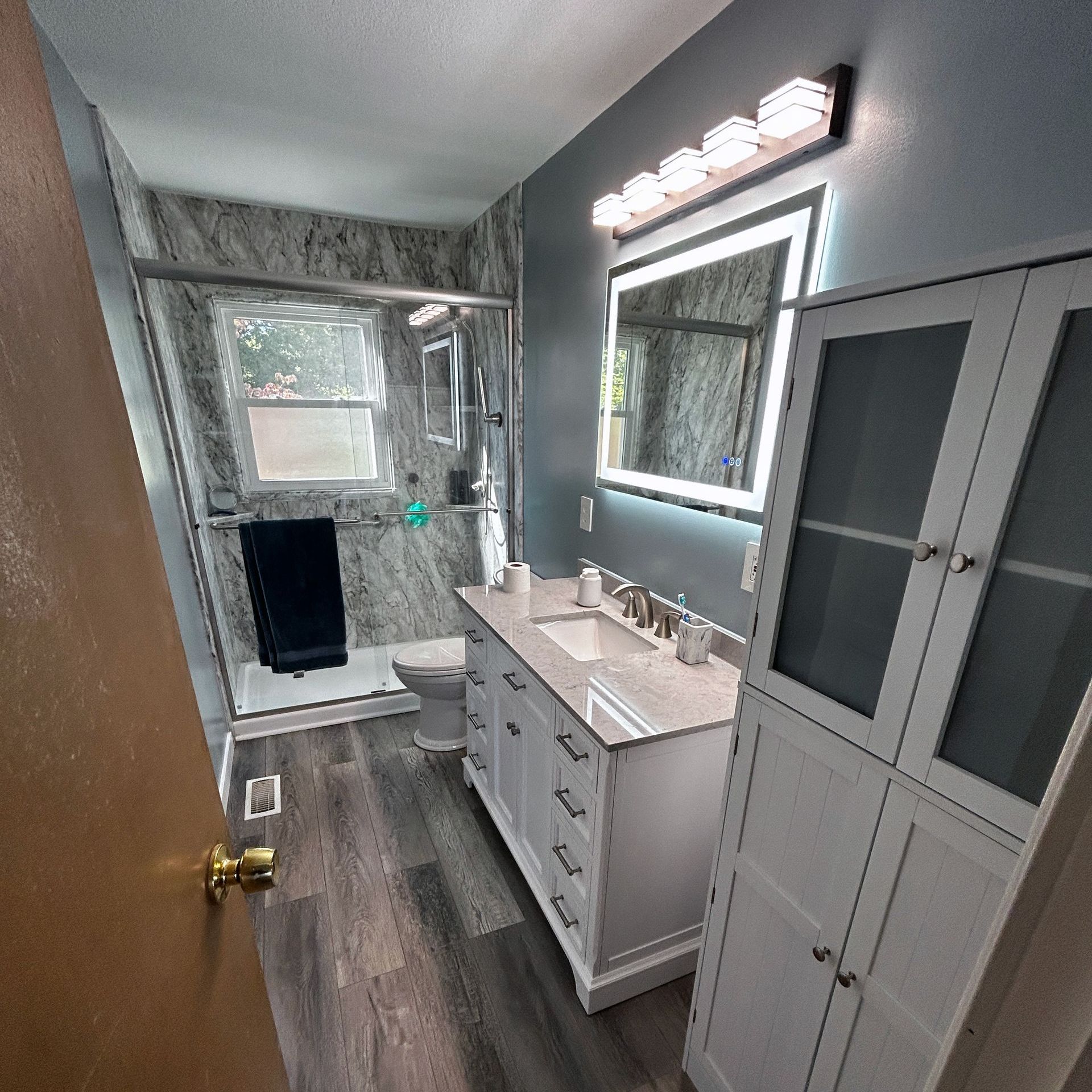 A bathroom with a sink , toilet , mirror and cabinets.