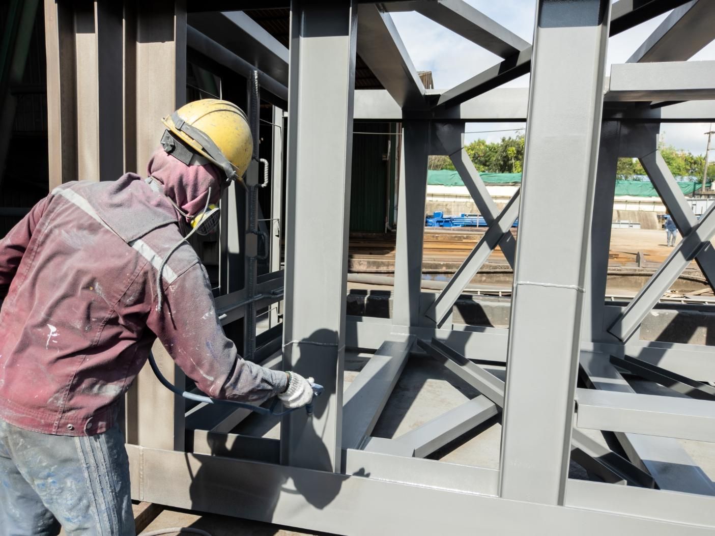 Construction Worker Spraying Gray Paint on a Metal Frame Structure, Outdoors — S D Maintenance In Point Clare, NSW