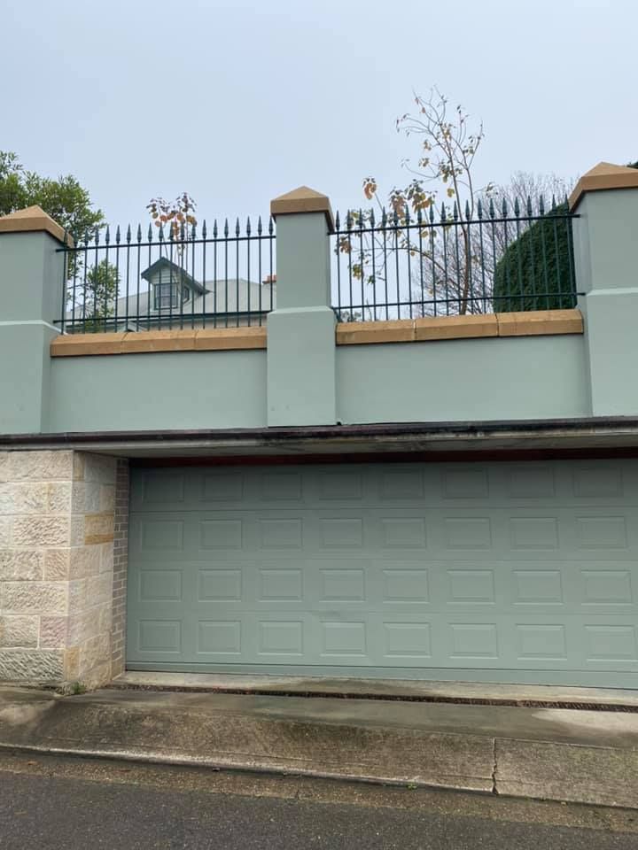 Garage with blue-green door beneath a pale blue wall topped with a black iron fence — S D Maintenance In Bateau Bay, NSW
