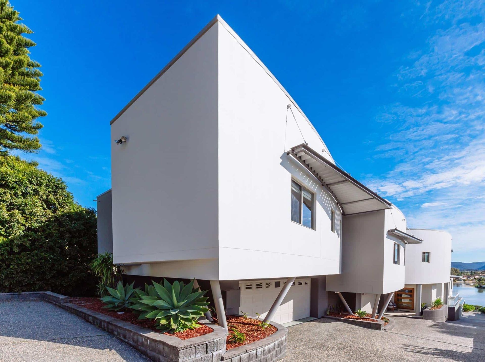 Modern white house with geometric shapes and angled supports, blue sky background. — S D Maintenance In Point Clare, NSW