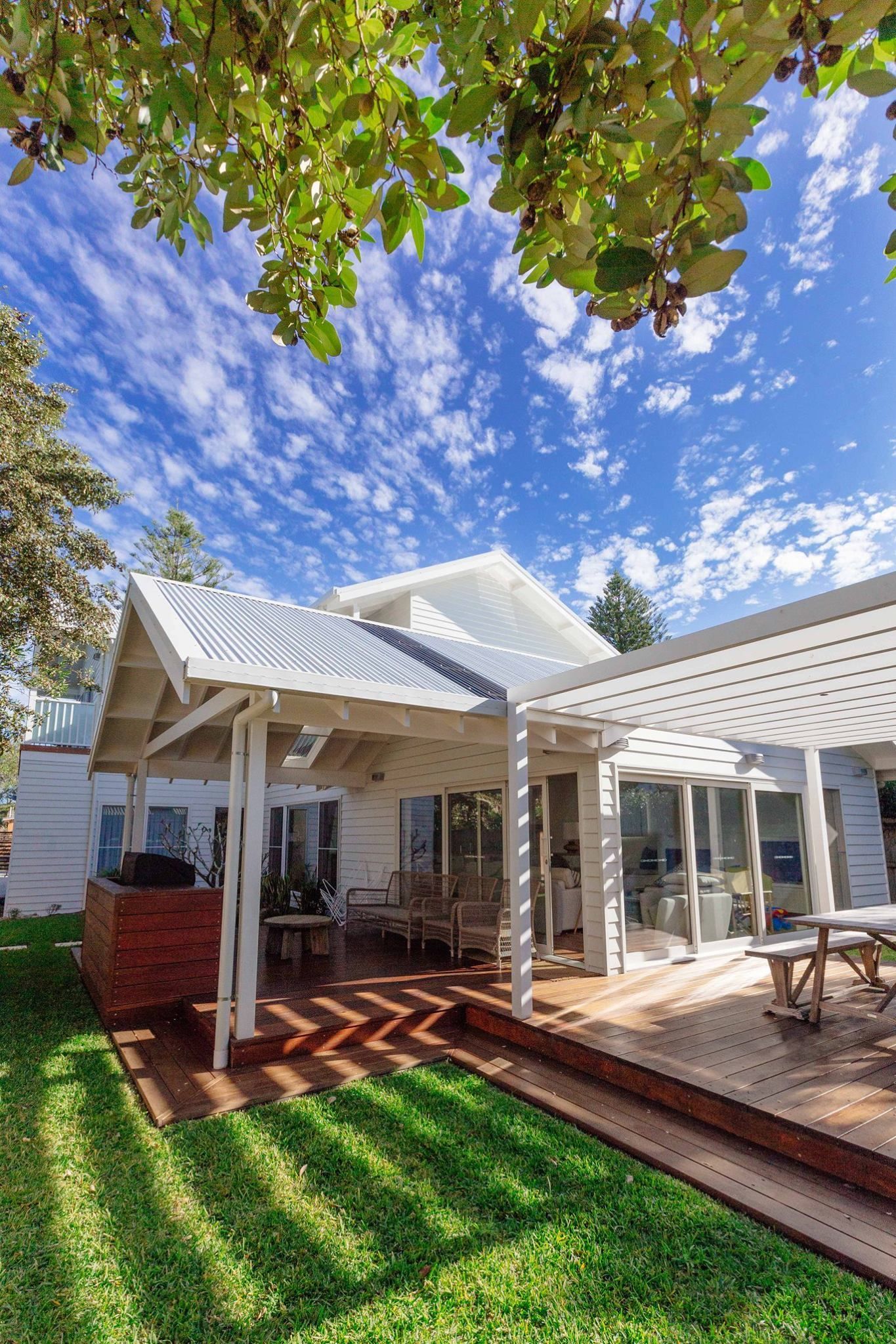 White house with wooden deck, pergola, and green lawn under a blue sky with fluffy clouds. — S D Maintenance In Point Clare, NSW