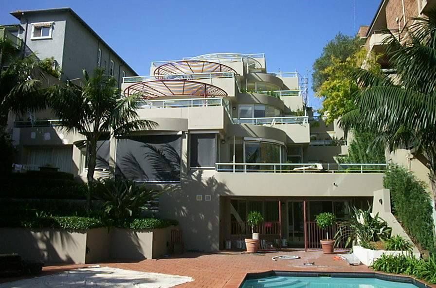 Multi-level beige building with balconies, pool, and palm trees under a sunny sky. — S D Maintenance In Point Clare, NSW