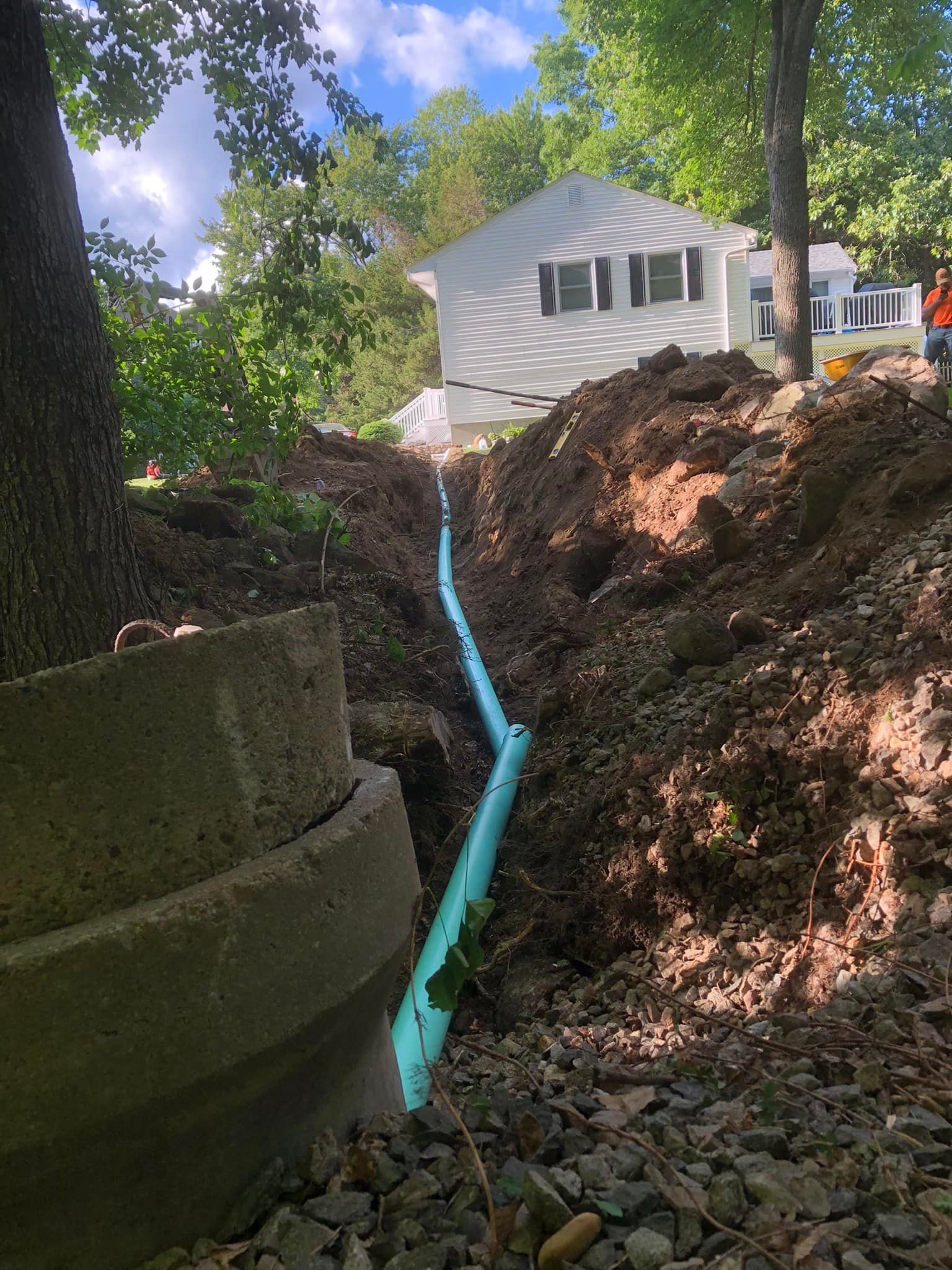 A drain pipe is being installed in the dirt in front of a house.