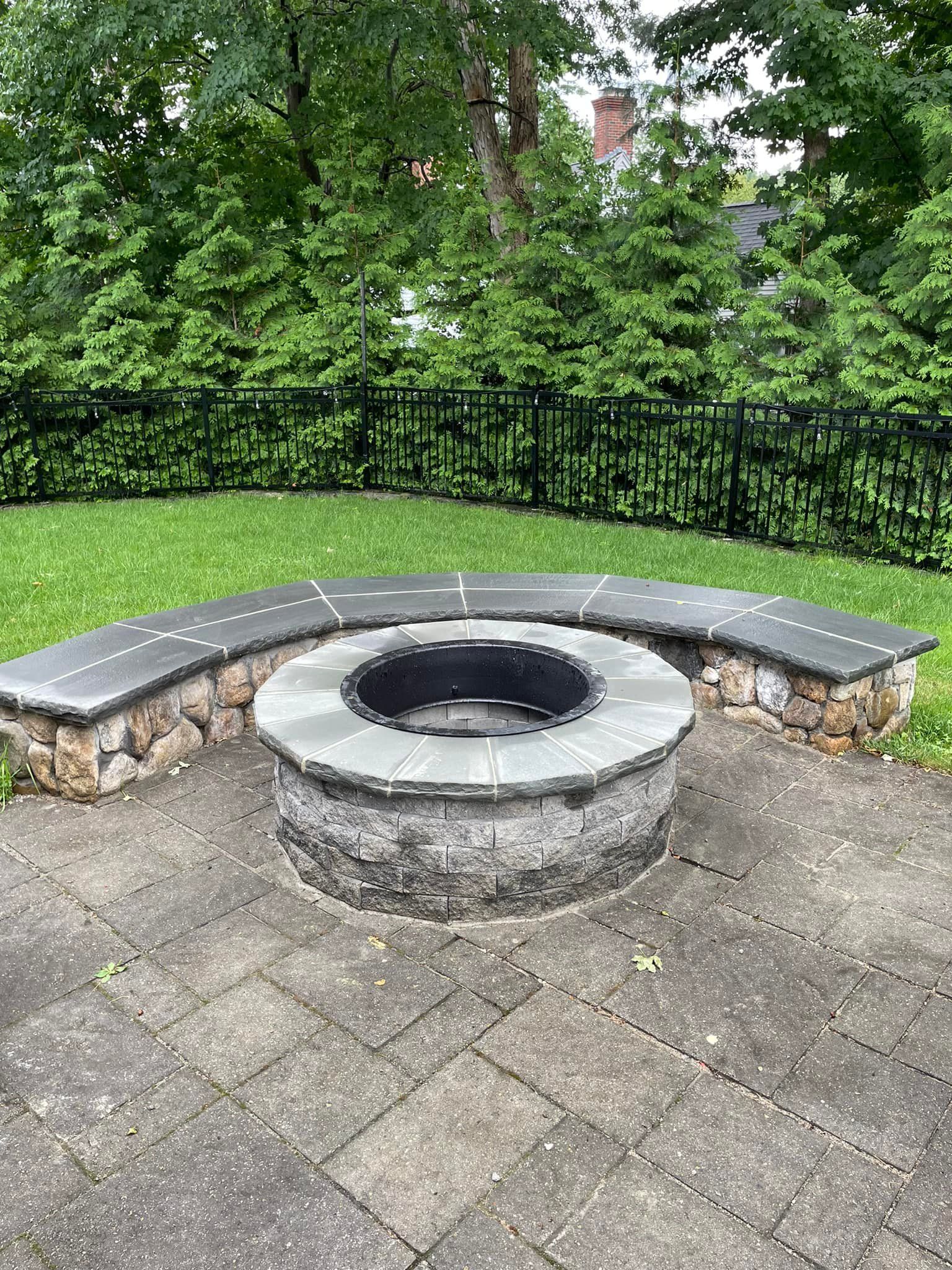 A fire pit is sitting on a patio next to a stone bench.