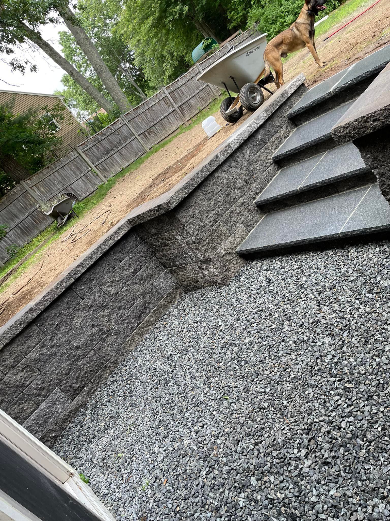 A person is standing on top of a pile of gravel next to a wheelbarrow.