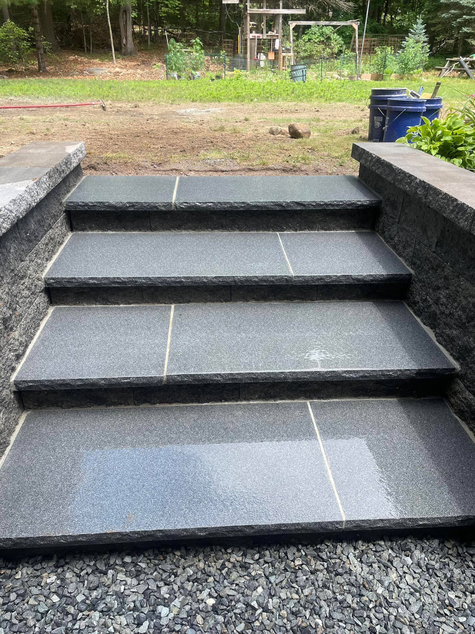 A set of black granite steps leading up to a gravel area.