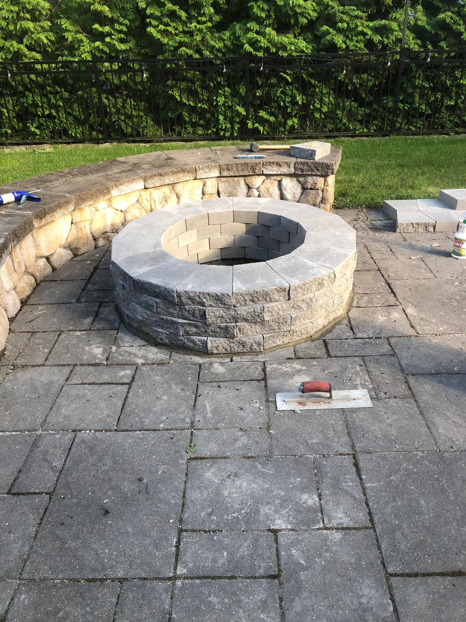 A fire pit is being built on a patio in a backyard.