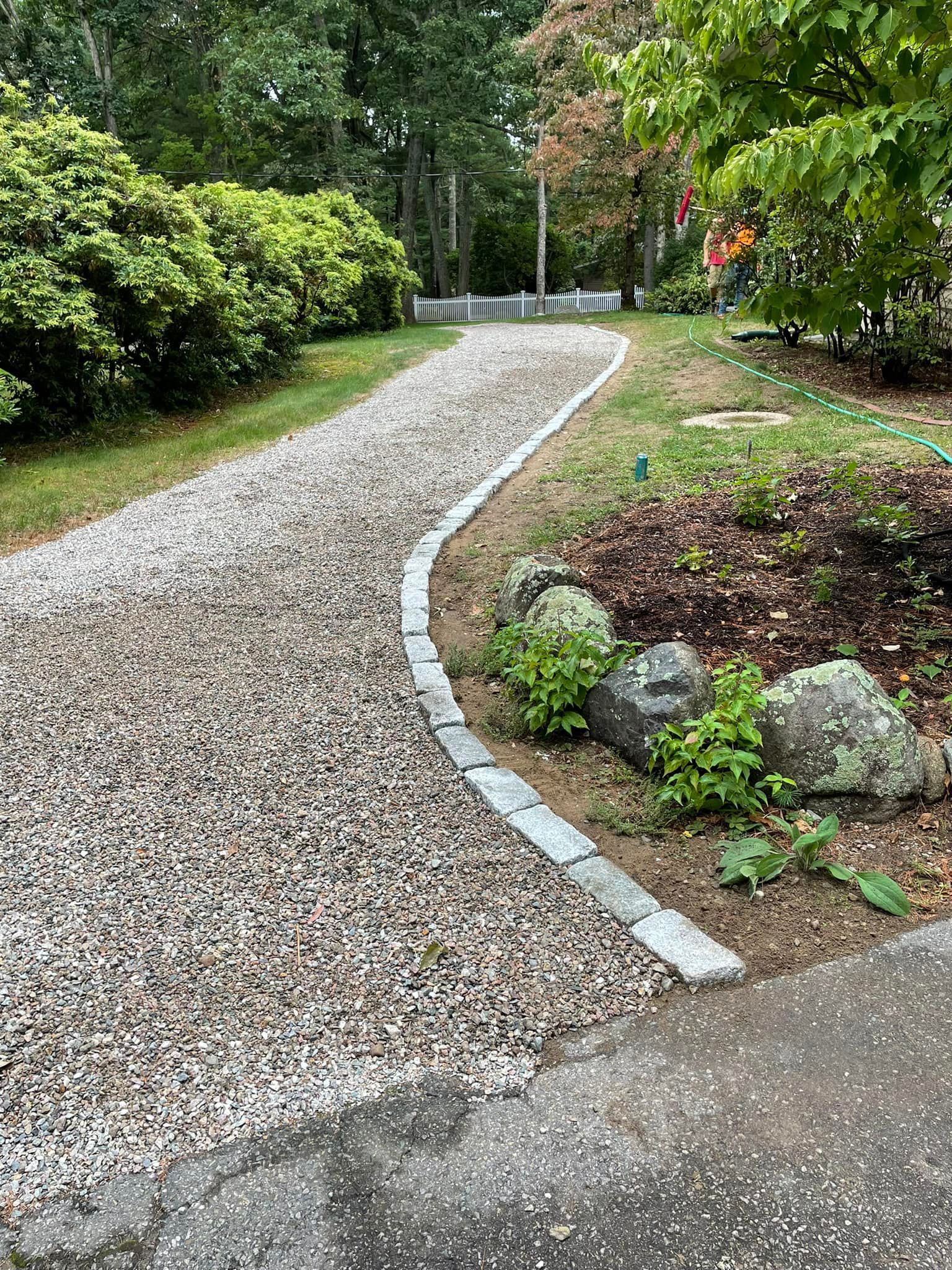 A gravel driveway leading to a house surrounded by trees and bushes.
