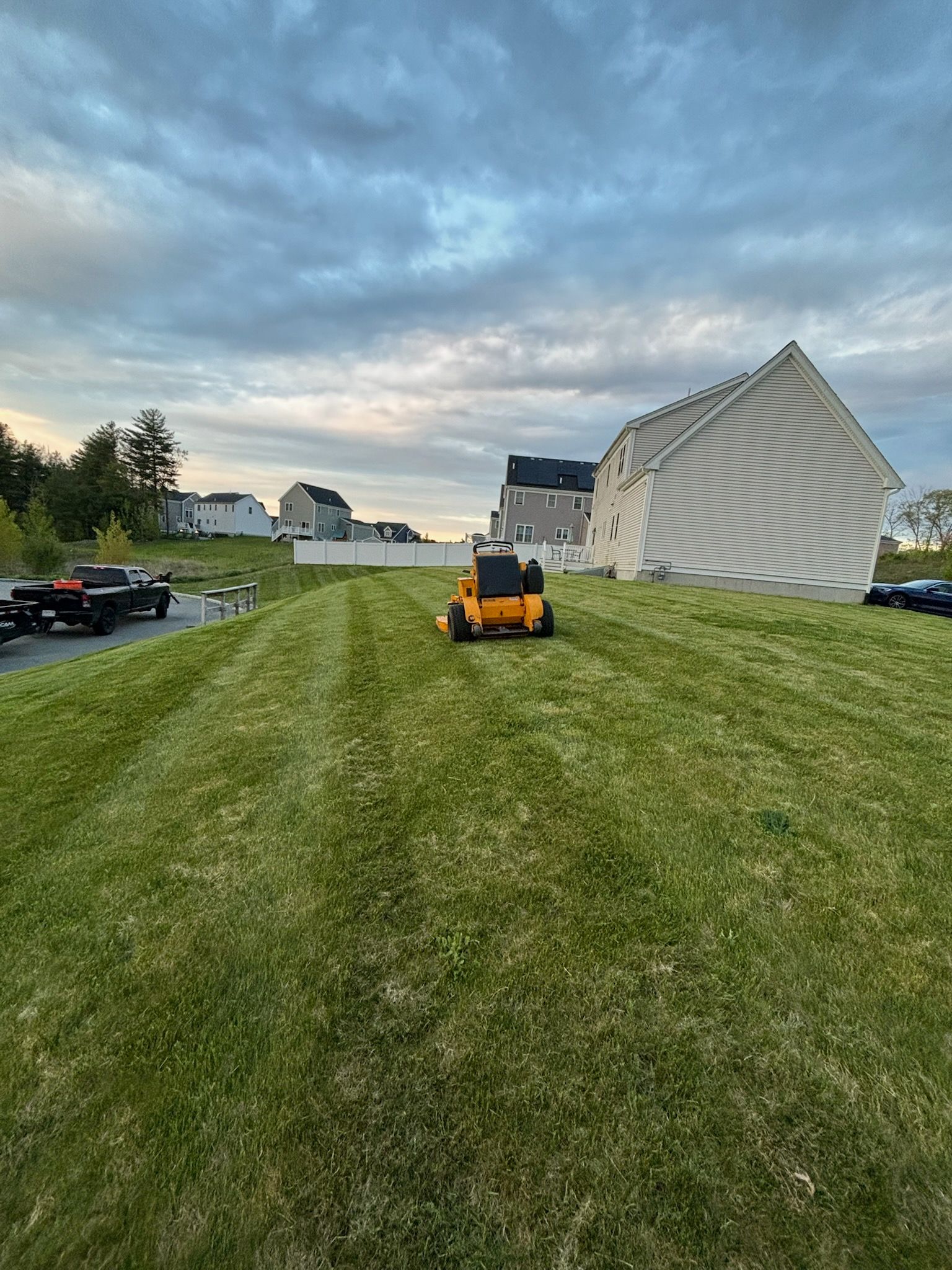 A yellow lawn mower is cutting a lush green lawn in front of a house.