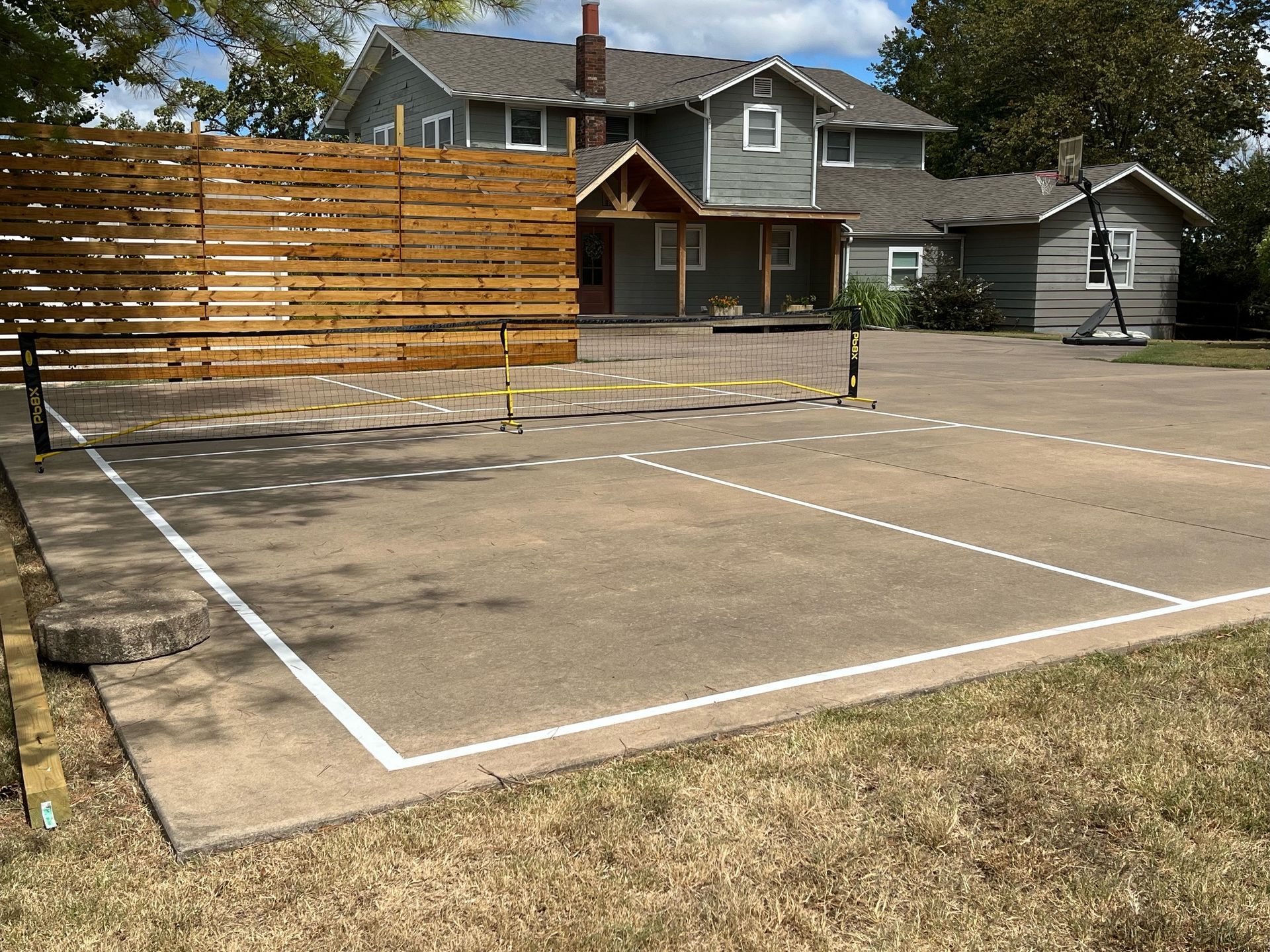 A tennis court in front of a house with a wooden fence