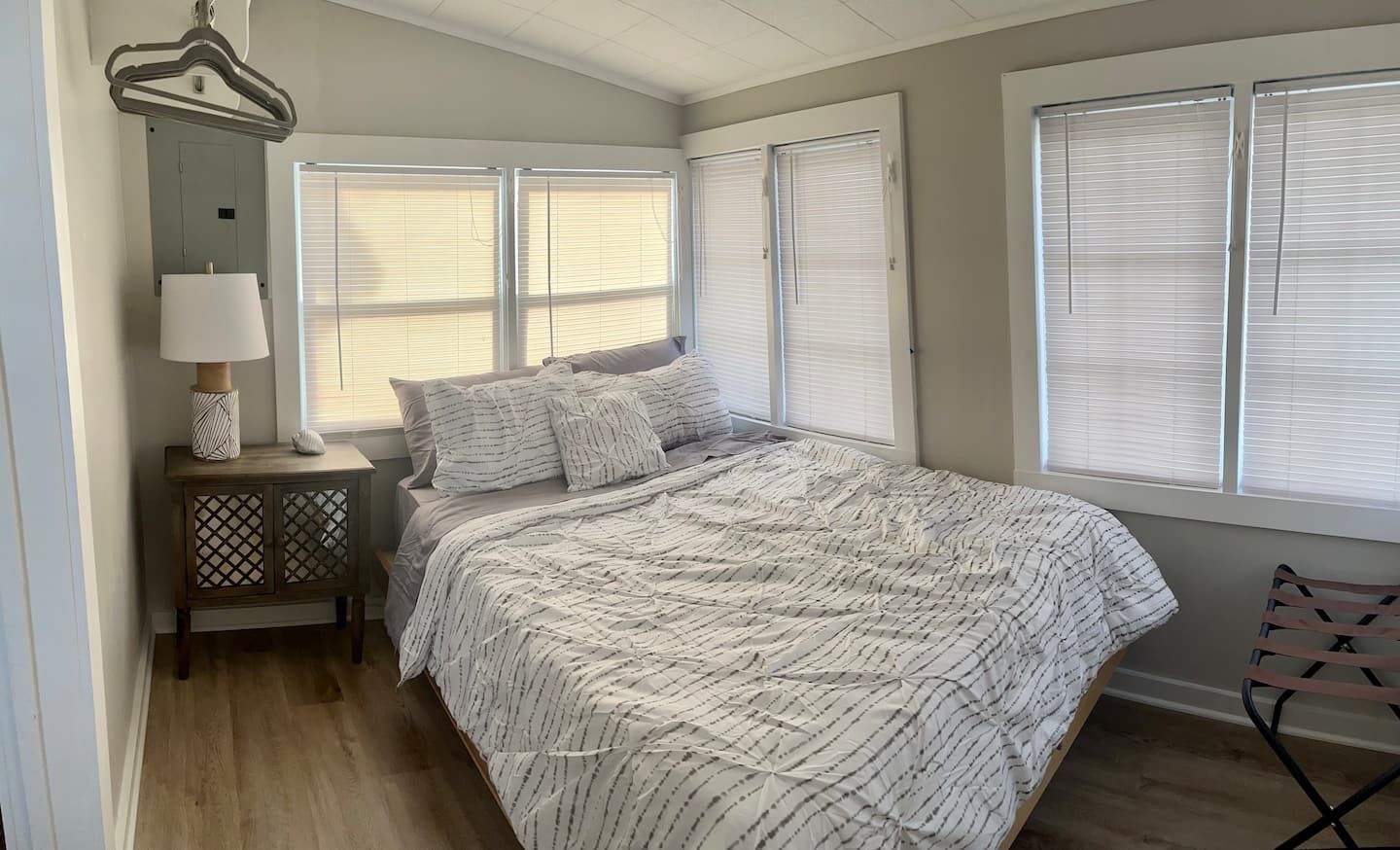 A bedroom with a bed , nightstand , lamp and two windows.