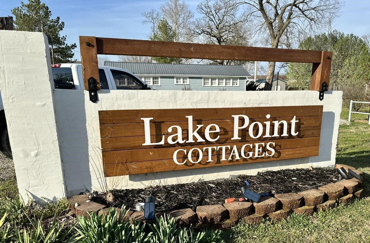 A wooden sign for lake point cottages is on a white wall.