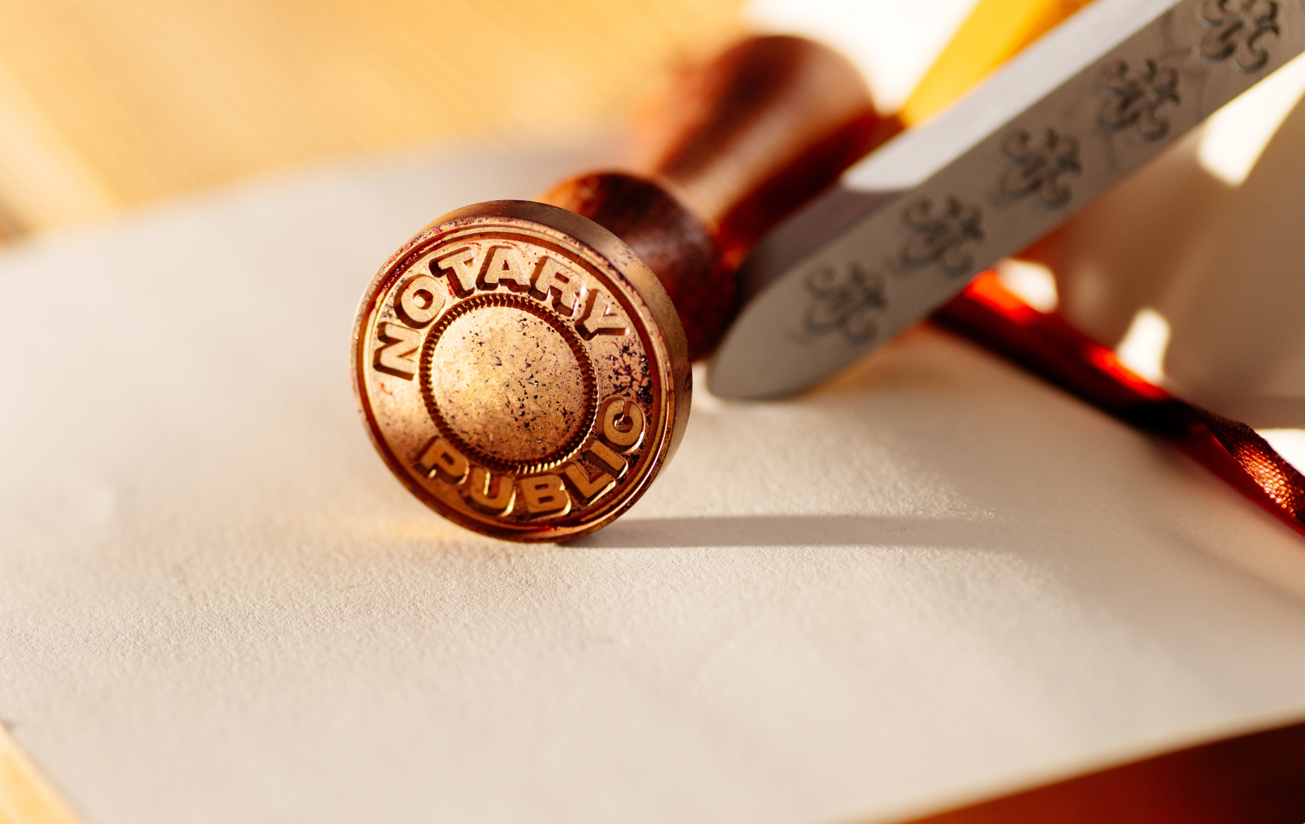 Bronze notary public seal on paper, alongside a wax seal with a red handle.