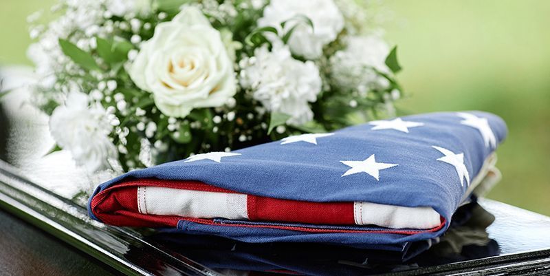 An american flag is laying on the hood of a limousine next to a bouquet of flowers.