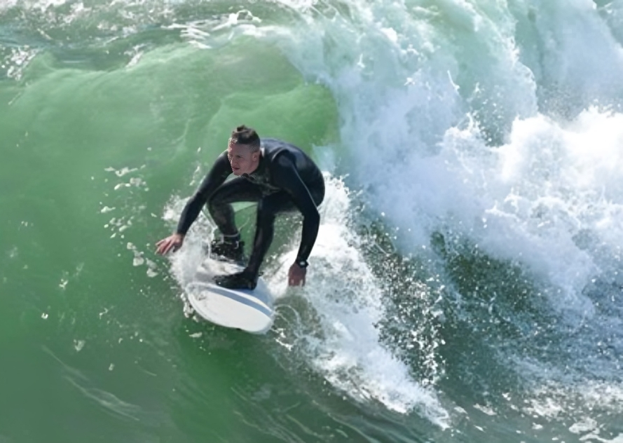 Surfer in black wetsuit rides a wave, balancing on a white surfboard. Surfer in black wetsuit rides a wave, balancing on a white surfboard.