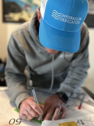 Person wearing a HydrFlow Irrigation hat writing on a map, with gray hoodie and a watch.