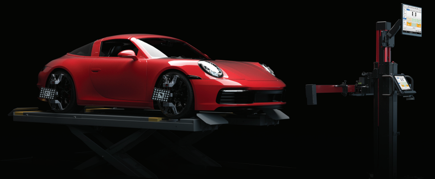 Red sports car being aligned on a lift in a dark garage.