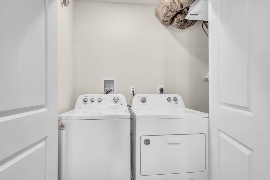 Laundry closet with a white washer and dryer under built-in shelves, viewed through open doors