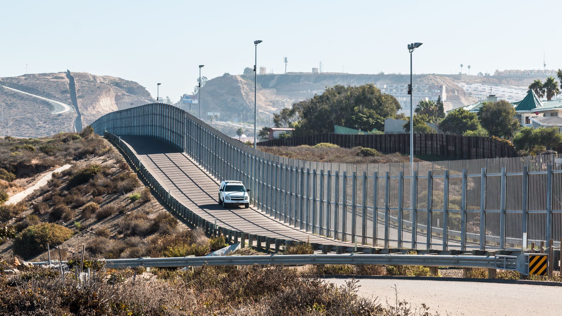 A car is driving down a road next to a fence.