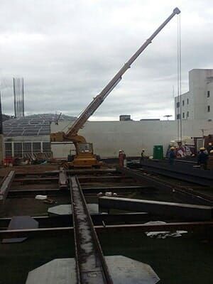 Una gran grúa está levantando una viga metálica en un sitio de construcción.