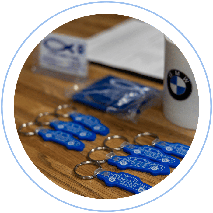 Blue car-shaped keychains displayed on the front desk, with a BMW mug and a Christian fish symbol sign in the background.