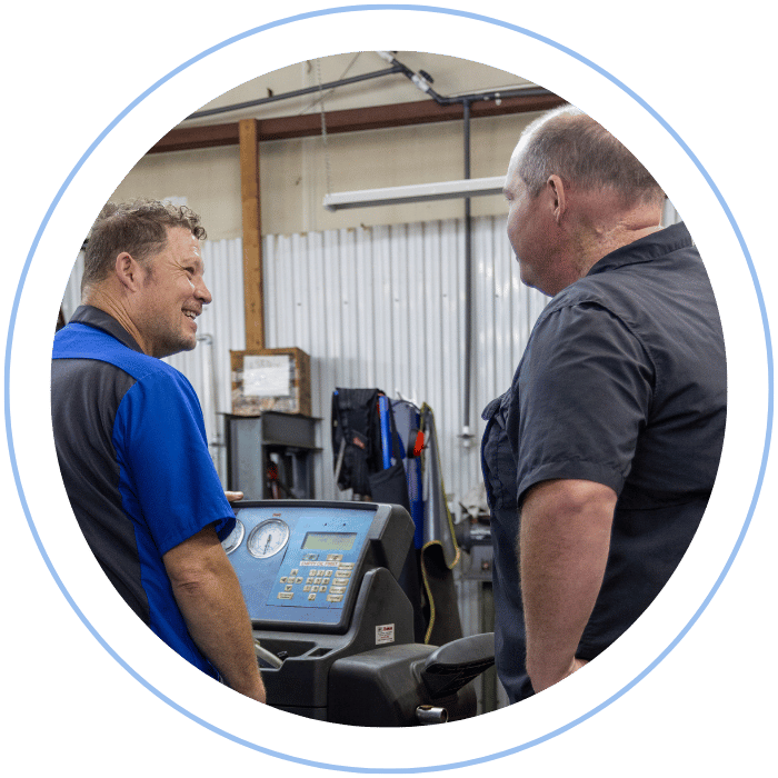OZ and Jonathan in uniforms stand in a workshop, smiling and talking while operating a technical diagnostic machine.