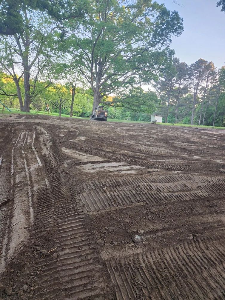 Dirt field with tractor tracks; trees in the background. Construction site.